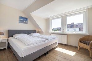 Une chambre à coucher comprenant un lit, une table de chevet, une chaise et une fenêtre donnant sur des immeubles.