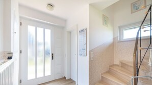 Ein Flur mit Holzboden, einer weißen Tür und einer Treppe mit Metallgeländer.