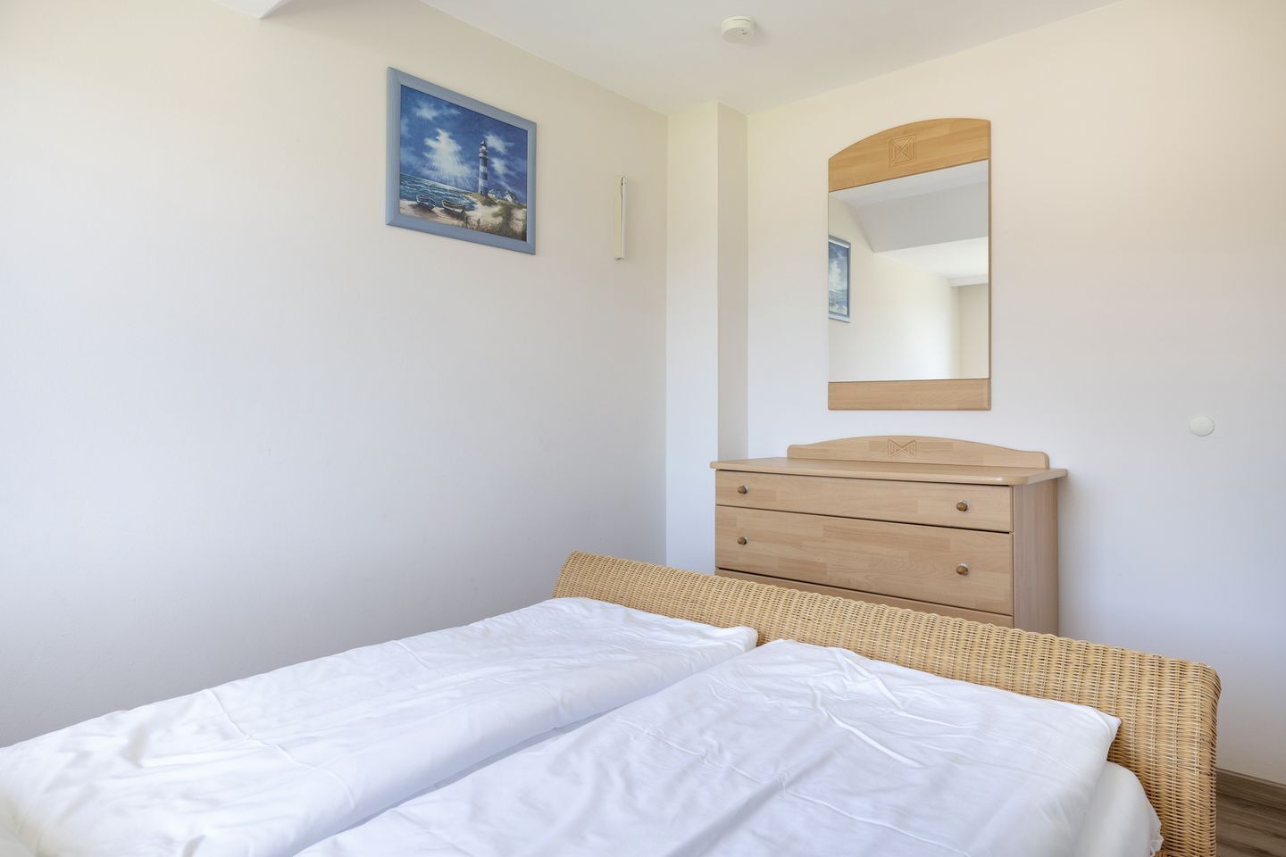 Ein Schlafzimmer mit einem Bett, einer hölzernen Kommode, einem Spiegel und einem Bild an der Wand.