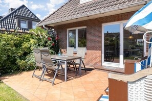 Une terrasse avec une table et des chaises, une maison en briques et un jardin.