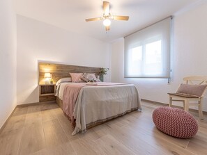 A bedroom with a bed, bedside table, lamp, window, and a chair.