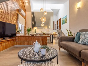 Een moderne woonkamer met een flatscreen-tv, een tafel met een patroon, een bank en een trap naar een verdieping erboven.