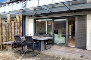 Une terrasse extérieure avec une table et des chaises, une terrasse en bois et une porte vitrée donnant sur un espace intérieur.