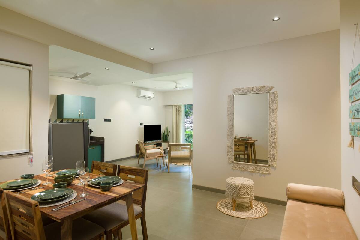 A dining area with a wooden table set for four, a sofa, and a television in the background.
