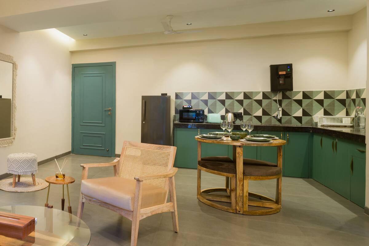 A modern kitchen with green cabinets, a round wooden table, and a blue door.