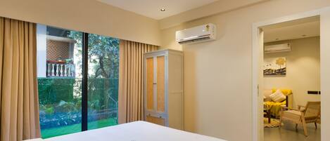 A hotel room with a bed, an air conditioning unit, a sliding glass door to a balcony, and a view of greenery outside.