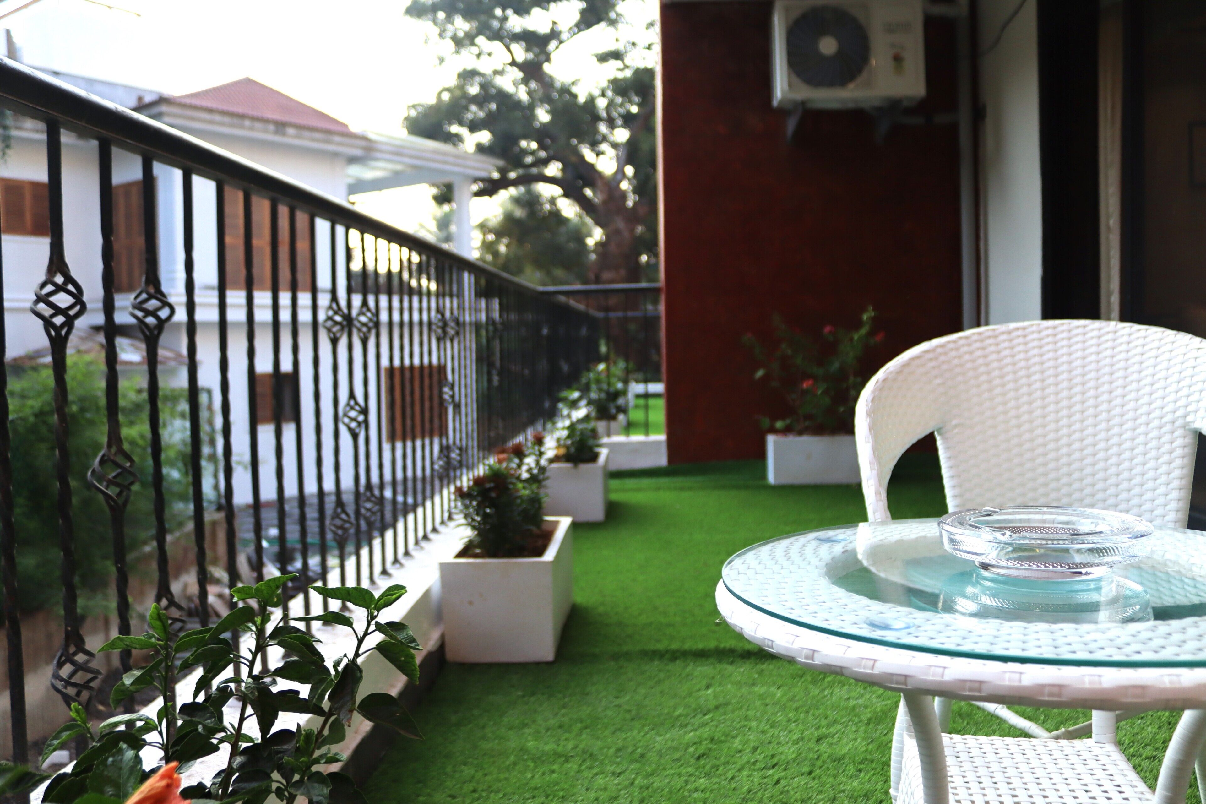 A balcony with a white wicker chair and a glass table, surrounded by potted plants and a metal railing.