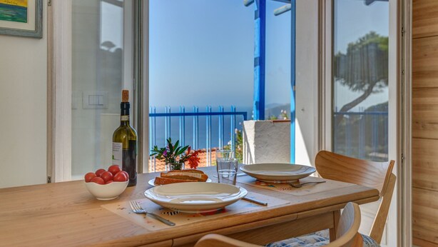 A dining table with a bottle of wine, a bowl of tomatoes, and a vase of flowers. - Bel Horizonte 7, Capoliveri (Capoliveri)