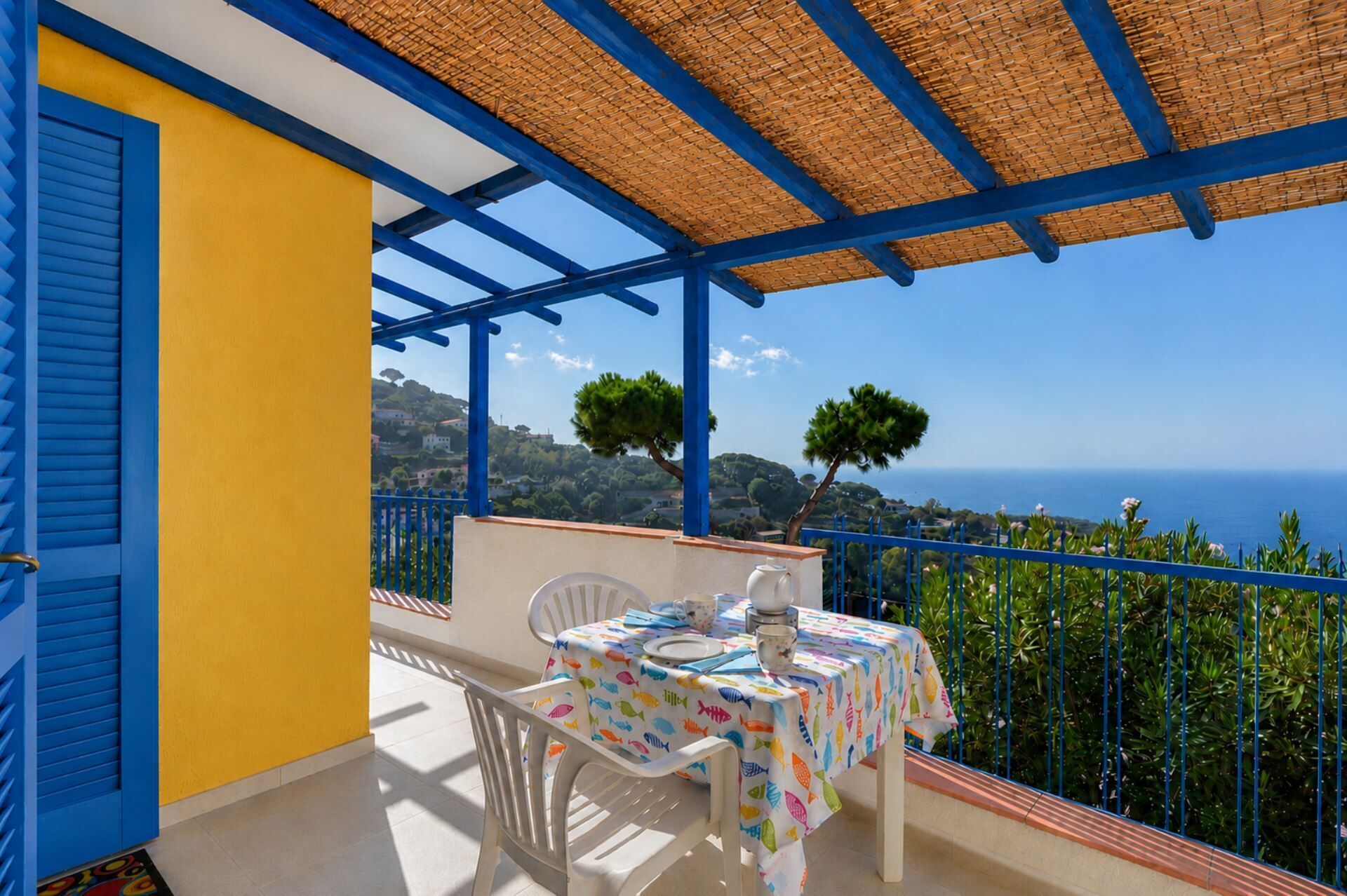 Ein Balkon mit Tisch für zwei Personen, einem blauen Geländer und Blick auf das Meer.