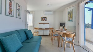 A modern living room with a teal sofa, a dining area with wooden chairs, a kitchen with a refrigerator, and a balcony with a view. - Bel Horizonte 7, Capoliveri (Capoliveri)
