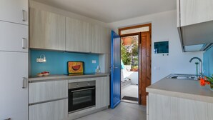 A modern kitchen with light wood cabinets, a built-in oven, and a blue-framed door leading to an outdoor area. - Bel Horizonte 7, Capoliveri (Capoliveri)