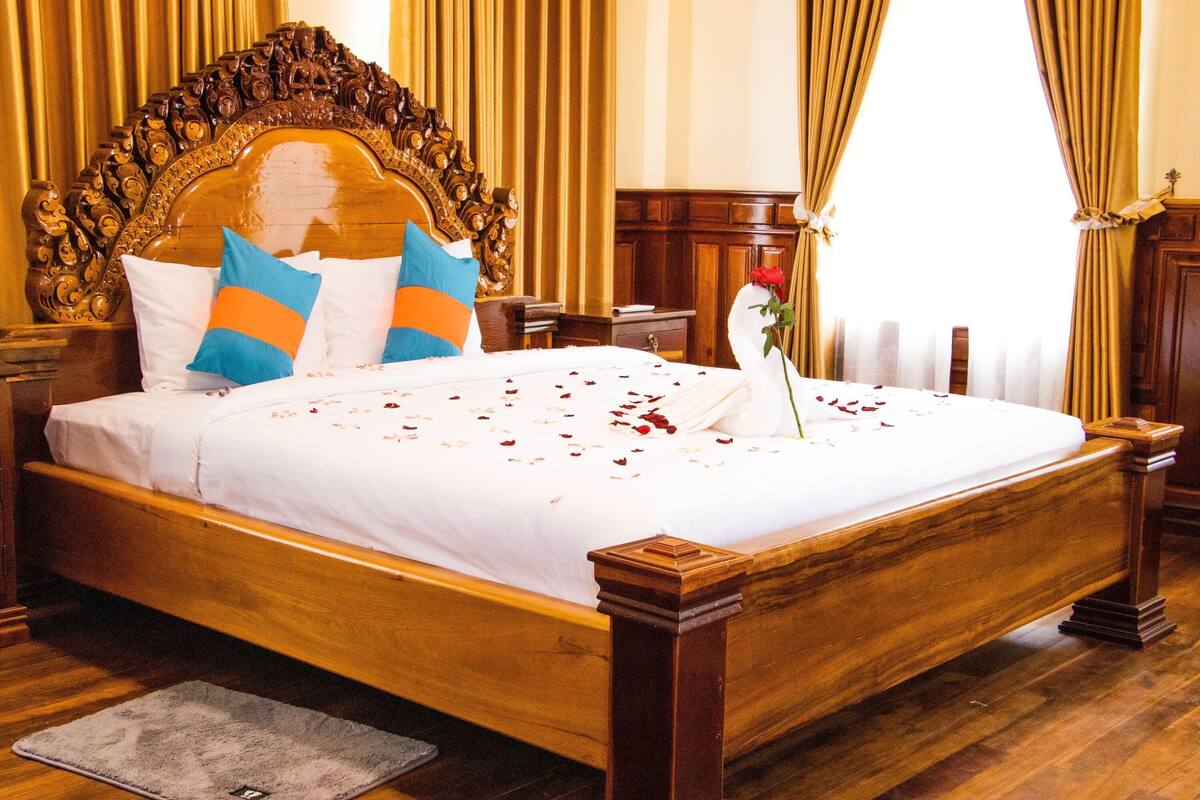 Un grand lit en bois avec une tête de lit sculptée, des draps blancs et des coussins bleus et orange.