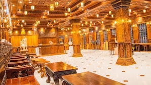 Een ruime hal met versierde houten zuilen en ingewikkelde plafonddecoraties, met rijen zitplaatsen en tafels.