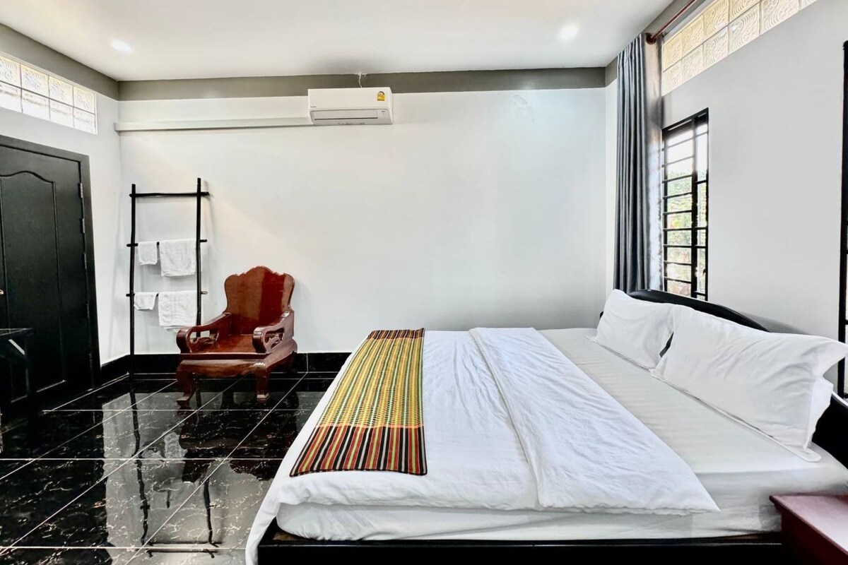 Een hotelkamer met een bed, een stoel, een handdoekrek en een raam.