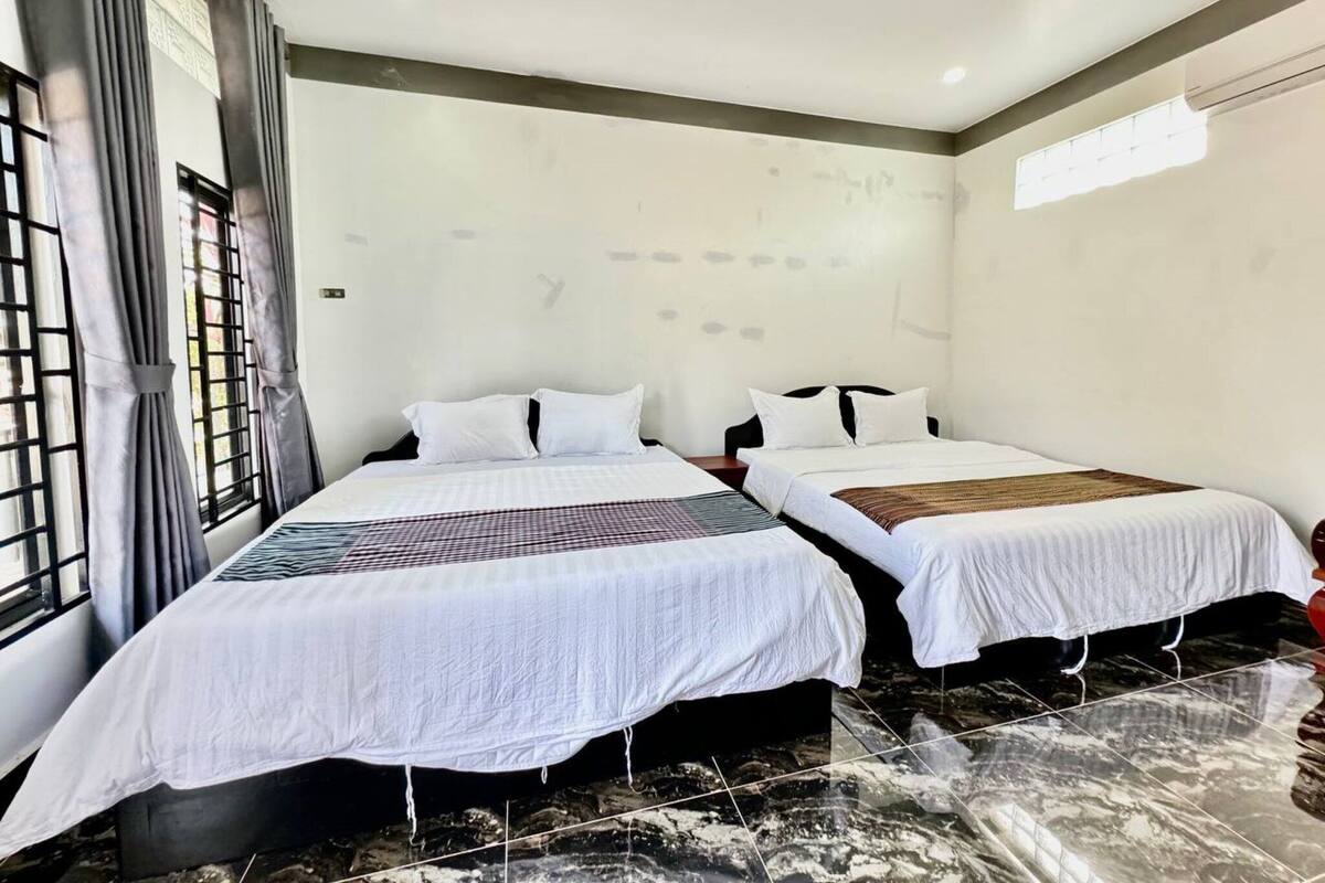 Une chambre d’hôtel avec deux lits, une grande fenêtre avec des rideaux et un sol en marbre.