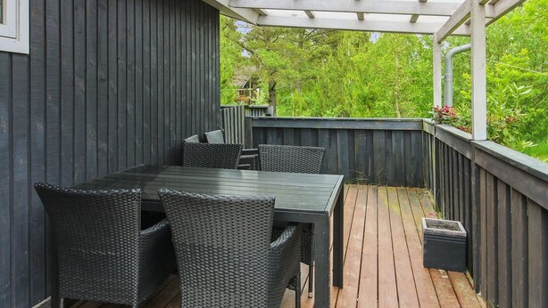 A covered outdoor patio with a wooden deck, dark-colored walls, and a table with chairs. - "Ylvi" - 2.8km from the sea by Interhome (Rømø)