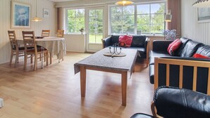 A spacious living area with a wooden table, a sofa, and a couch. There are large windows providing natural light and a view of greenery outside. - "Ylvi" - 2.8km from the sea by Interhome (Rømø)