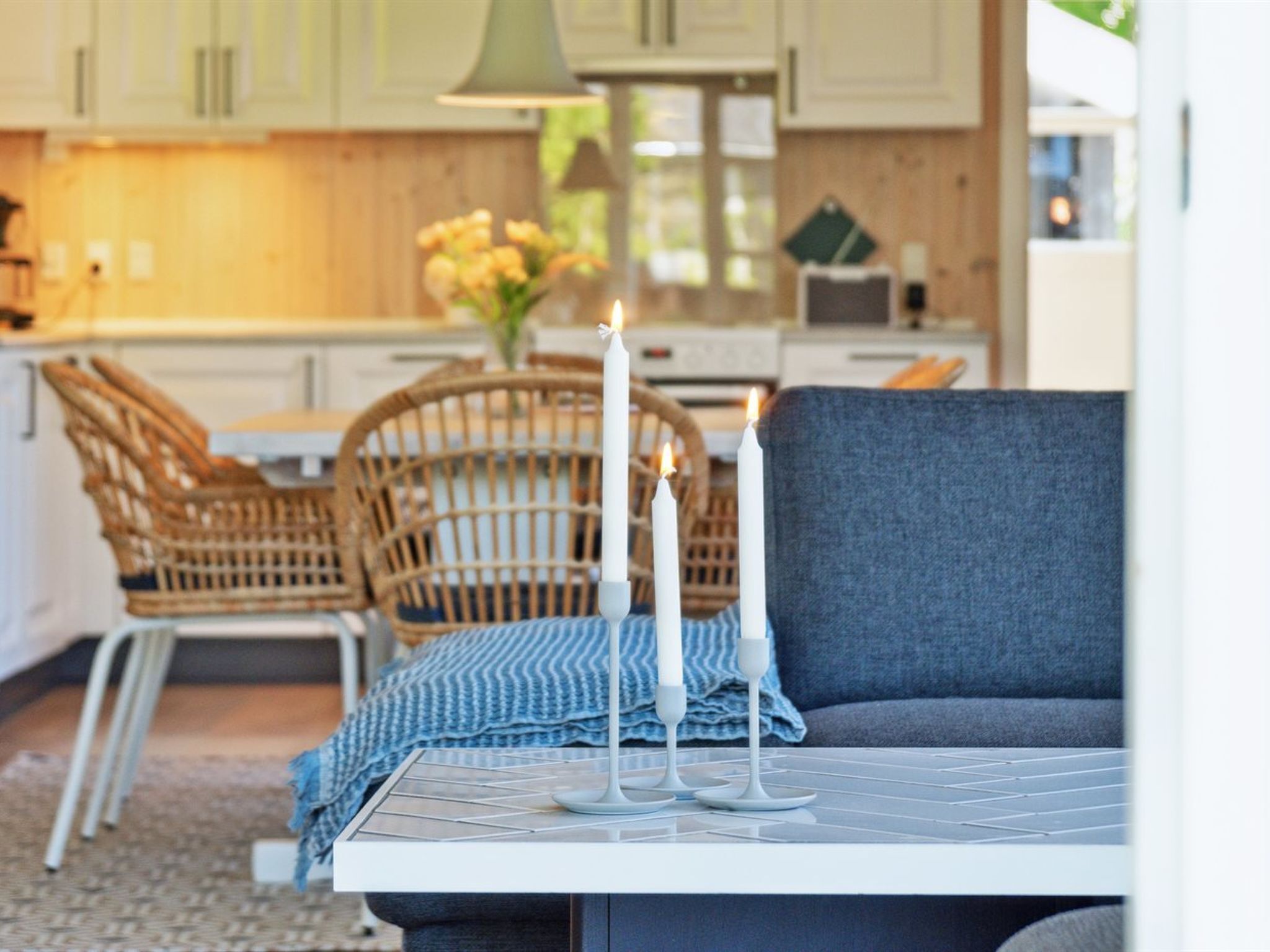 Una cocina moderna con armarios blancos, una zona de comedor con sofá azul y una mesa, y una silla de mimbre.