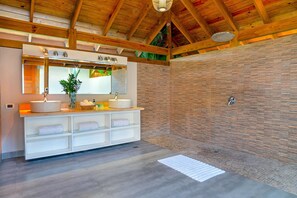 A modern bathroom with a stone shower wall, a large mirror, and a white vanity with a sink and towel storage.