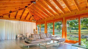 A spacious living room with a wooden ceiling, large windows, a beige sofa, and a glass coffee table.