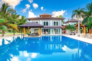 A large swimming pool with a house in the background, surrounded by palm trees and clear skies. - Srvittinivillas Agp36 / Spacius / Confortable Luxury Villa/ Family/ Team/ Cdc (La Romana)