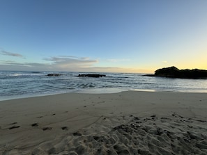 Ein Strand mit Fußspuren, die zum Wasser führen, einem Felsen und einem klaren Himmel.