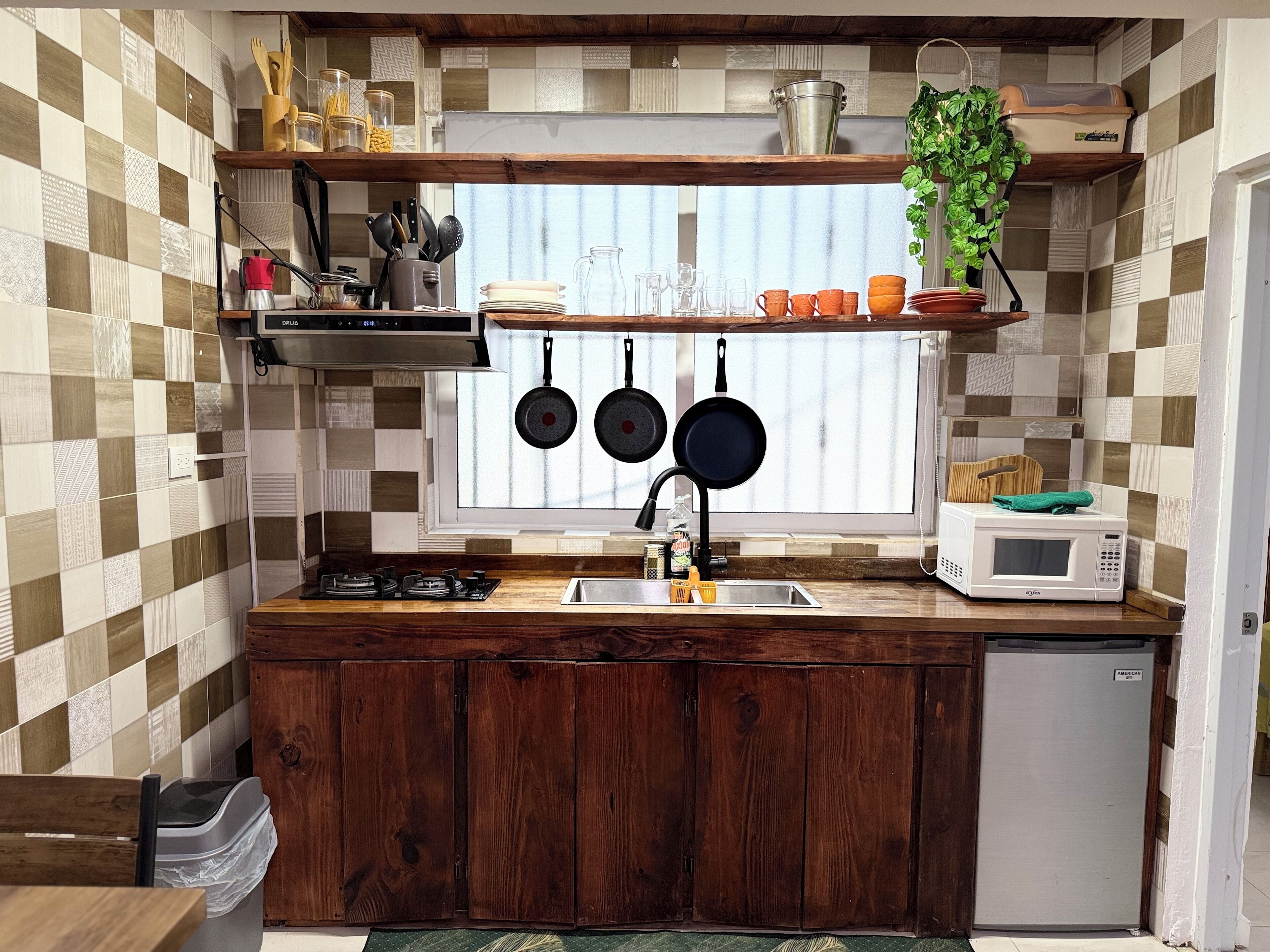 A kitchen with a checkered tile backsplash, wooden cabinets, a window with a view, and a microwave on the counter.