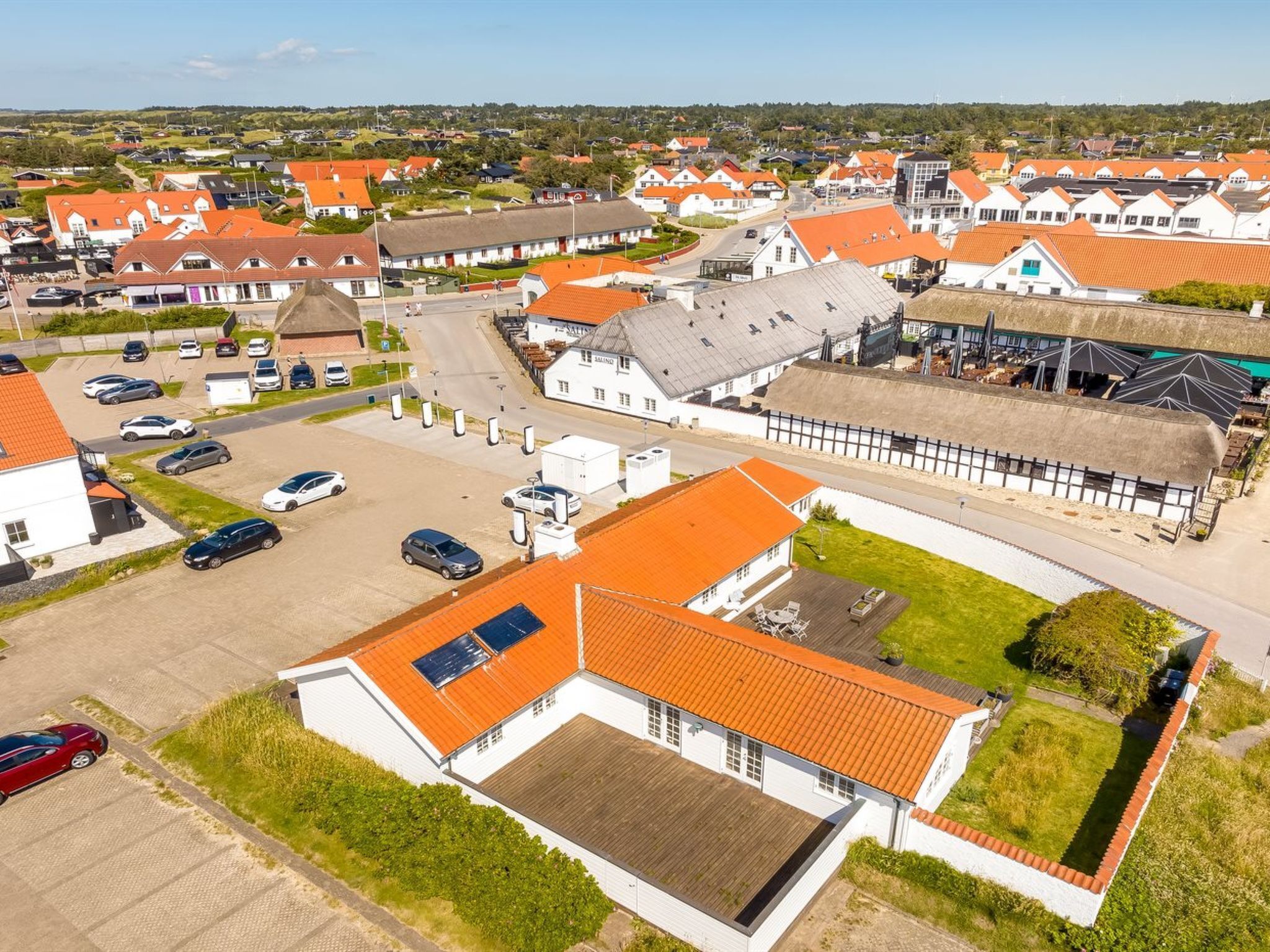 A residential area with houses featuring red-tiled roofs, a central road, and a parking lot with several cars.