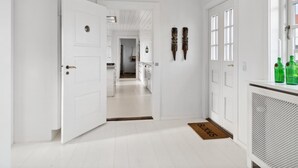 Een gang met witte wanden, een houten plafond en een deur die naar een keuken leidt.