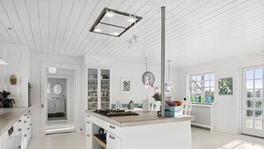 Een ruime keuken met witte kasten, een centraal eiland en uitzicht op het buitenleven door grote ramen.
