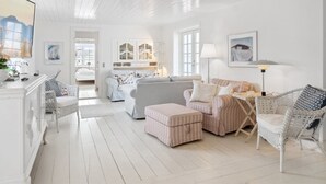 Een ruime woonkamer met een wit kleurenschema, met een bank, fauteuils en een salontafel.