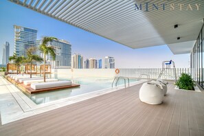 A rooftop pool area with lounge seating, a lifeguard stand, and a view of the city skyline.