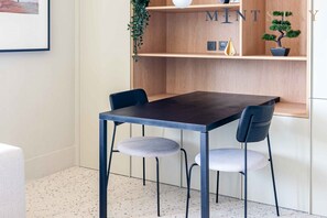 Un coin repas moderne avec une table en bois foncé et deux chaises, une petite plante en pot et une étagère ornée d’objets décoratifs.