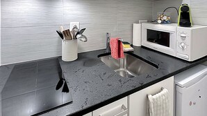 A modern kitchen with white cabinets, a black countertop, a stainless steel sink, and a microwave. - Studio 505 - Sion Old City - Swiss Alps (Sion)