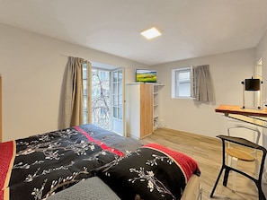 Une chambre à coucher comprenant un lit, un bureau, une chaise, une armoire et une fenêtre avec des rideaux.