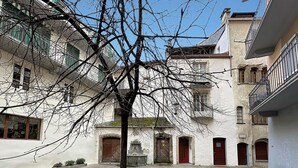 A courtyard with a tree in the center, surrounded by buildings with balconies and doors. - Studio 505 - Sion Old City - Swiss Alps (Sion)