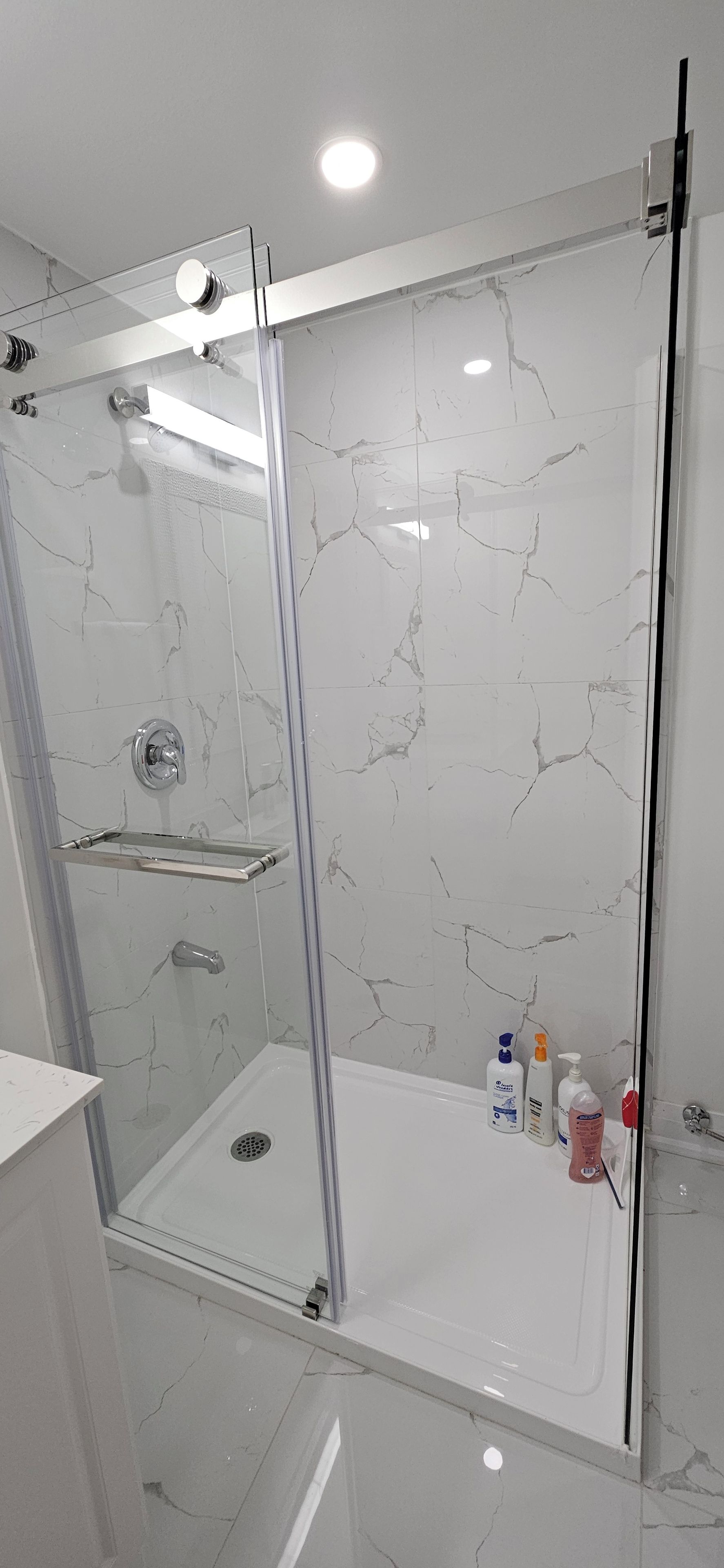 A modern shower with a glass door, a built-in shelf, and a showerhead.