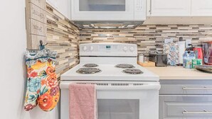 A kitchen with a white stove, a microwave above it, and a tiled backsplash. There are cabinets and a countertop with various items on it. - Mississauga 2BDR Lower Unit Parking Self-check in (Mississauga)