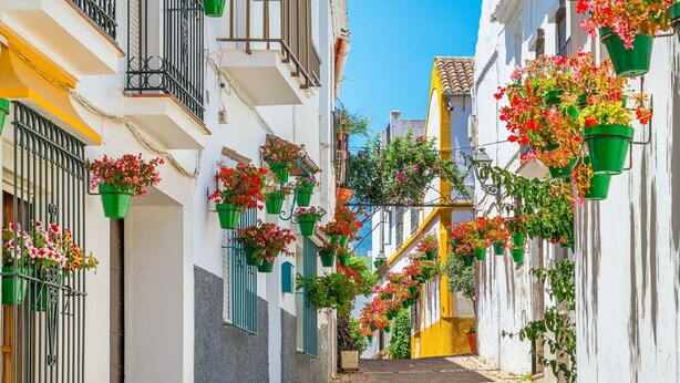 A narrow street with white buildings, balconies with green railings, and flower pots hanging from the railings. - Experience sophistication in this contemporary four-bedroom frontline golf townhouse (San Roque)
