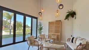 A spacious living room with large windows, wicker furniture, and hanging pendant lights. - Experience sophistication in this contemporary four-bedroom frontline golf townhouse (San Roque)