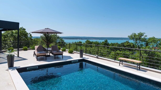 Une piscine avec vue sur la mer, deux chaises longues, un banc et une pergola avec un parasol.