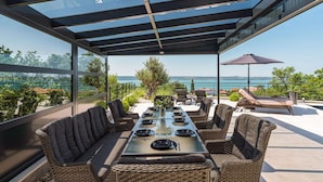 Une terrasse sur le toit dotée d’un espace repas fermé par des baies vitrées, de sièges extérieurs et offrant une vue sur la mer.