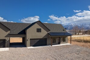 Une maison moderne à deux étages, dotée d’un garage, d’un porche couvert et offrant une vue sur des montagnes enneigées en arrière-plan.