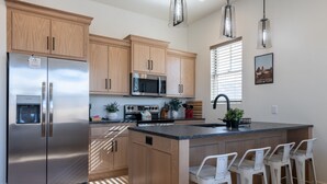 Eine moderne Küche mit Holzausstattung, Edelstahlgeräten, einer zentralen Kochinsel mit Barhocker und Pendelleuchten.