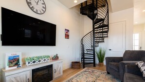 Ein Wohnzimmer mit Flachbildfernseher, Kamin, Treppe und einer Couch.