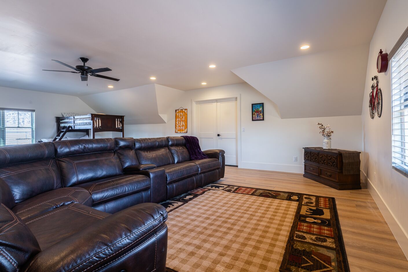 A spacious living room with a leather sectional sofa, a ceiling fan, recessed lighting, a staircase, and a decorative rug.