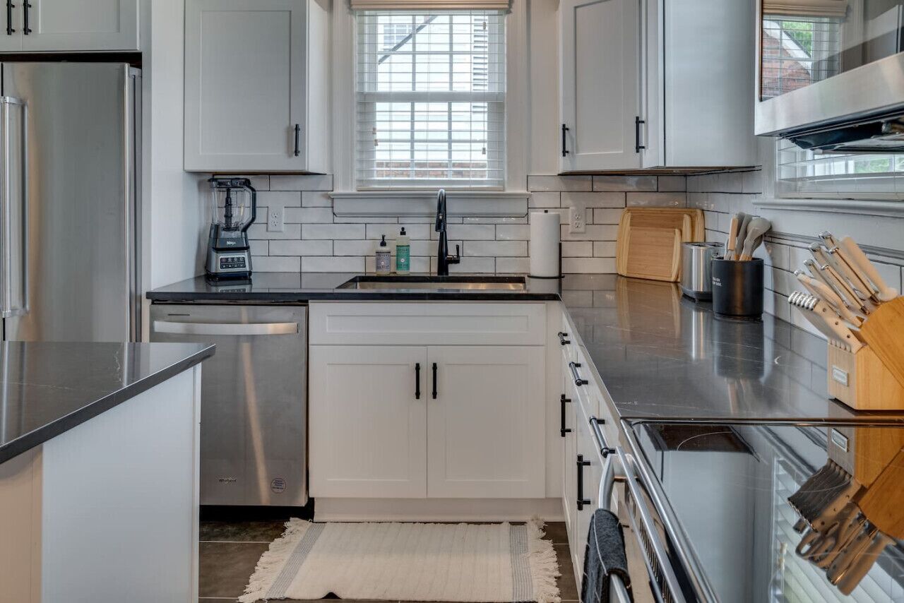 A modern kitchen with white cabinets, a stainless steel refrigerator, a built-in dishwasher, and a large window above the sink.