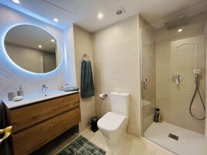 Une salle de bain moderne avec un meuble-lavabo en bois, un miroir rond, des toilettes et une douche à parois de verre.