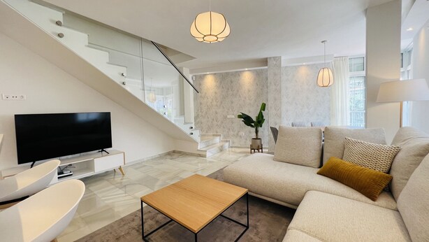 A modern living room with a flat-screen TV, a wooden coffee table, a sofa with cushions, and a staircase with glass railings. - 3010 Spacious Luxury Family Apartment in Marbella's Heart (Marbella)