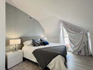 Une chambre à coucher avec un lit, une table de chevet, une lampe et une fenêtre avec des rideaux.